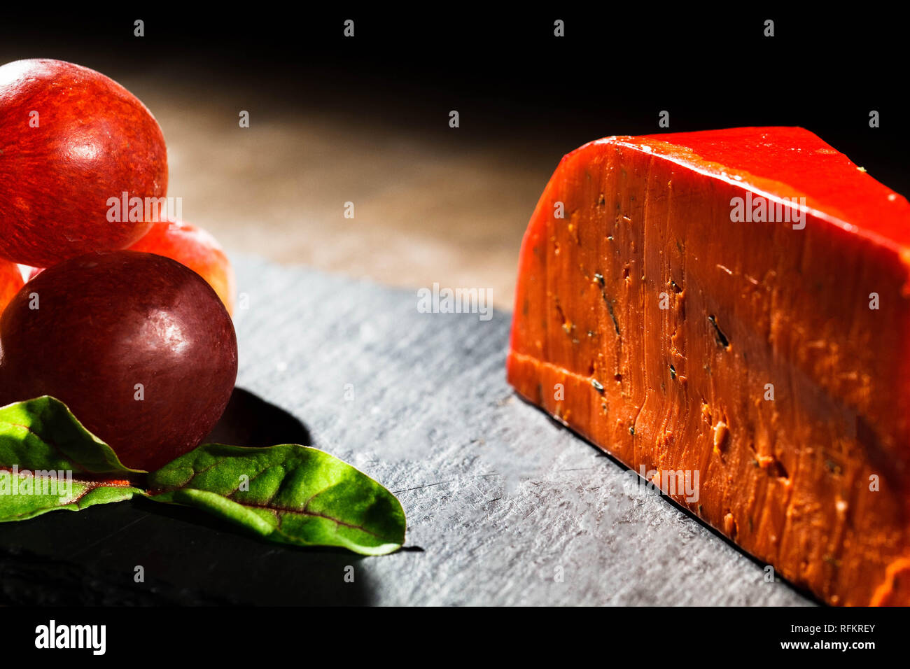 Pink grape berries lie before orange piece of cheddar Stock Photo