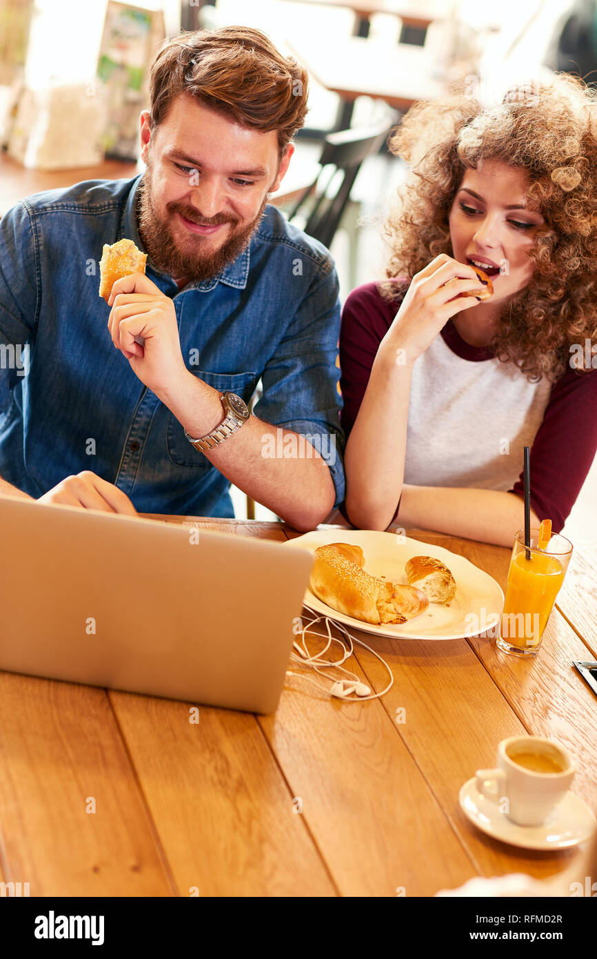 Male and female looking at laptop and eat croissant in restaurant Stock Photo