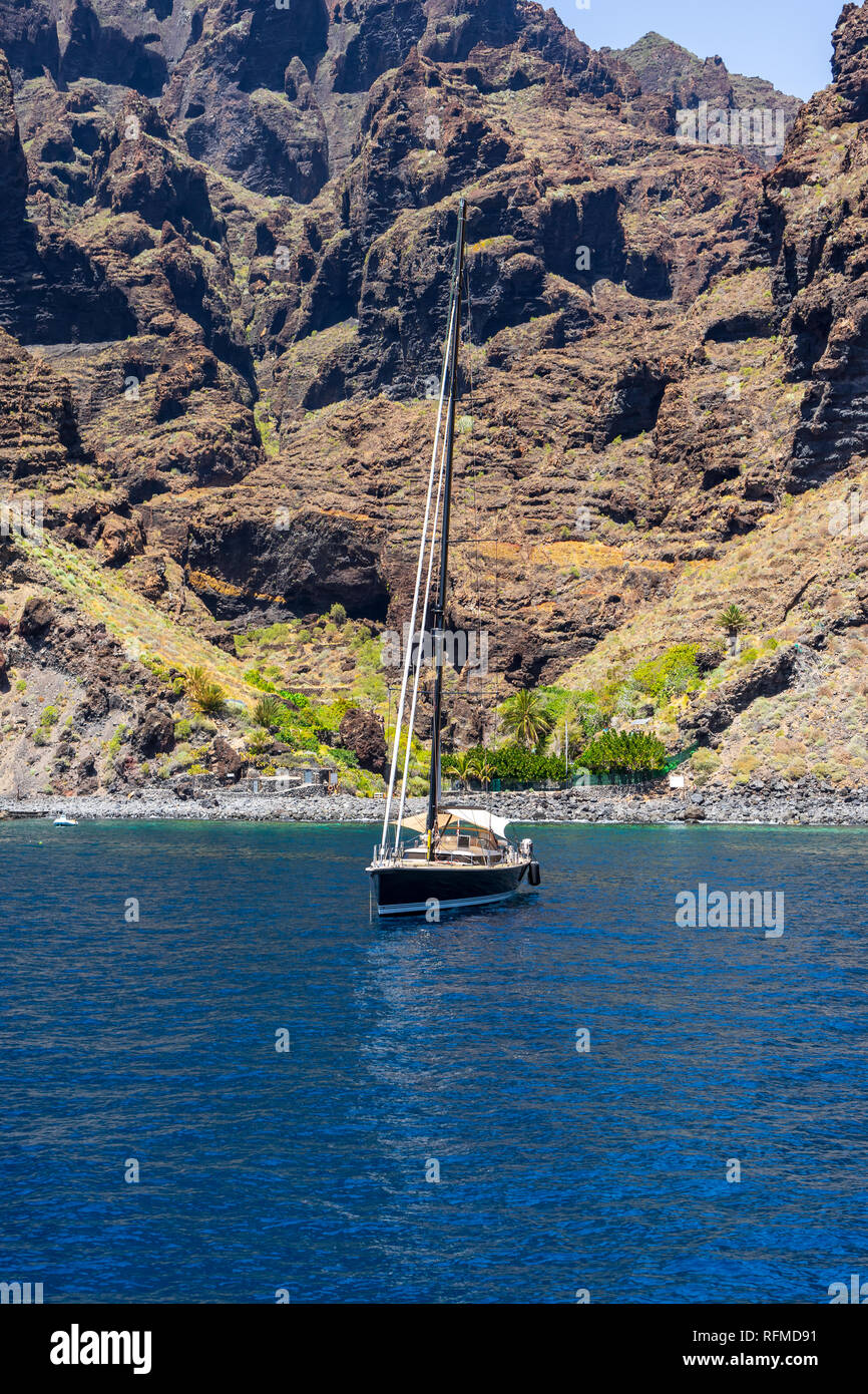 Yachts and boats of tourists near the vertical cliffs Acantilados de Los Gigantes (Cliffs of the Giants). View from Atlantic Ocean. Stock Photo