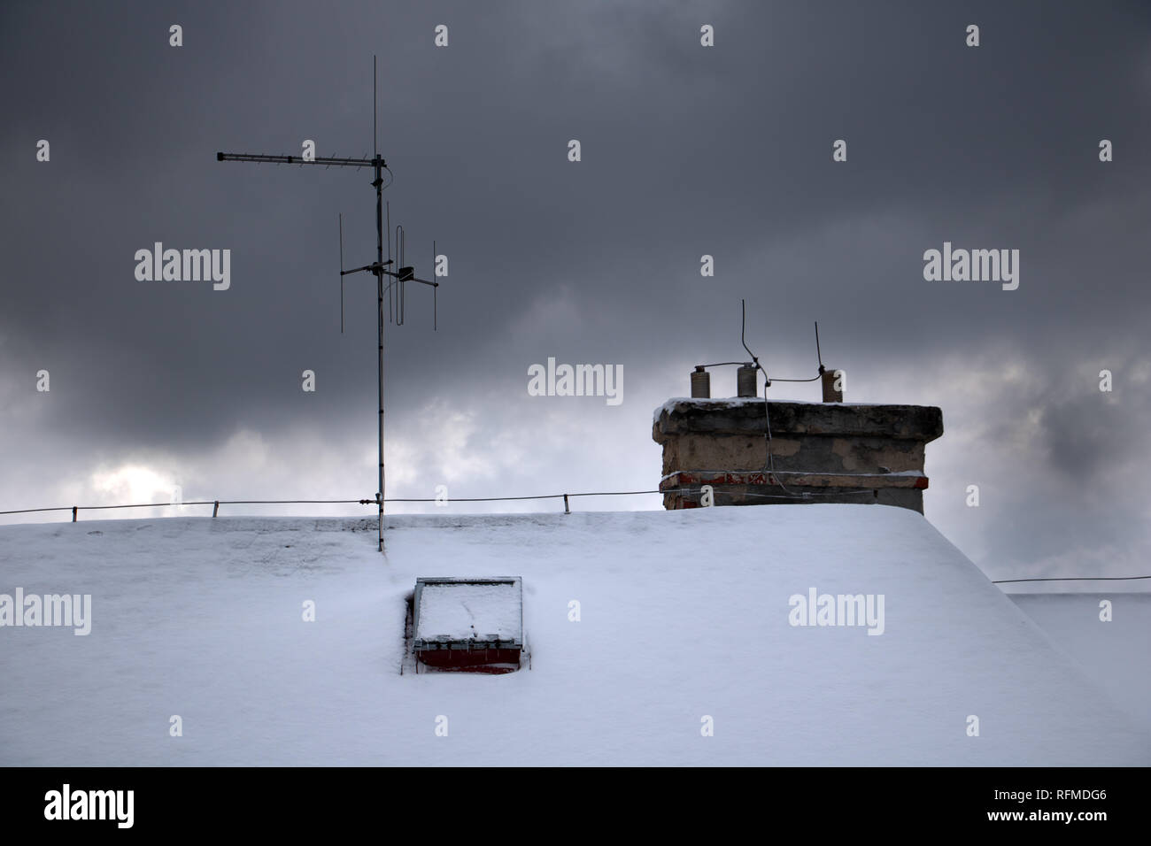 An antenna silhouette on an evening winter sky with clouds. Clouds over the snowy roof with a chimney and an antenna. Stock Photo