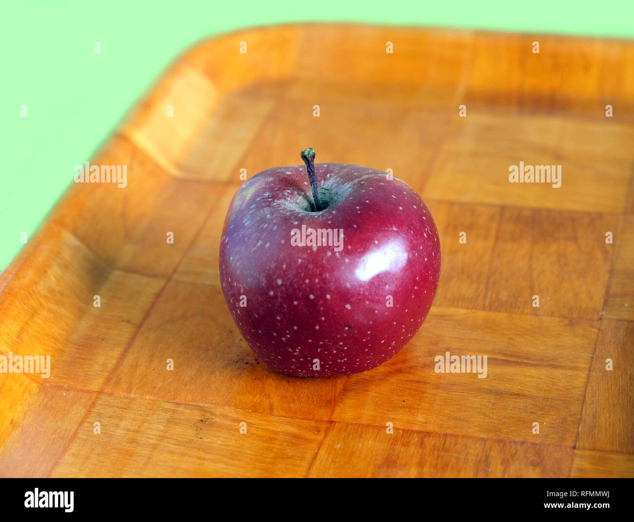 Still life with ripe red apple on brown wooden tray side view isolated