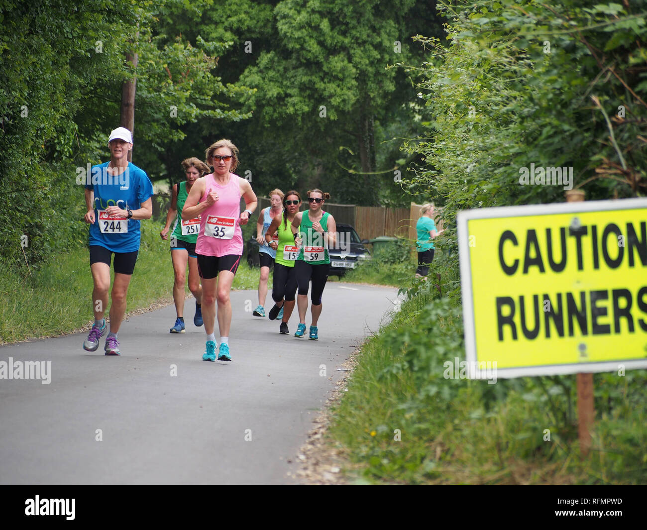 Female runners taking part in a ladies road running race with a 'caution runners' sign on the road Stock Photo
