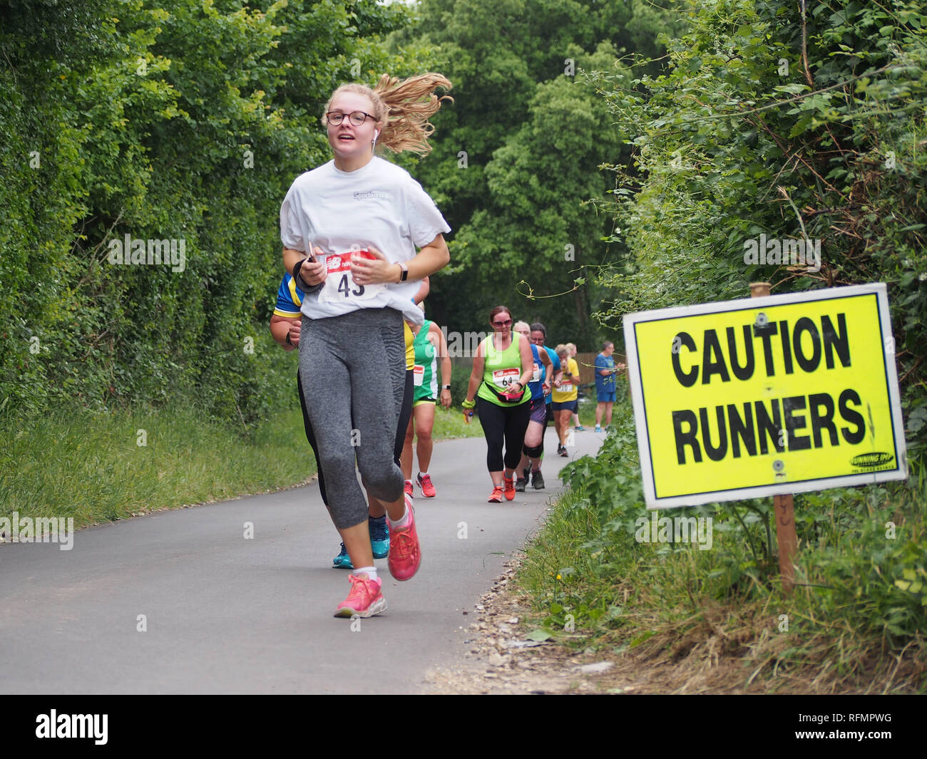 Female runners taking part in a ladies road running race with a 'caution runners' sign on the road Stock Photo