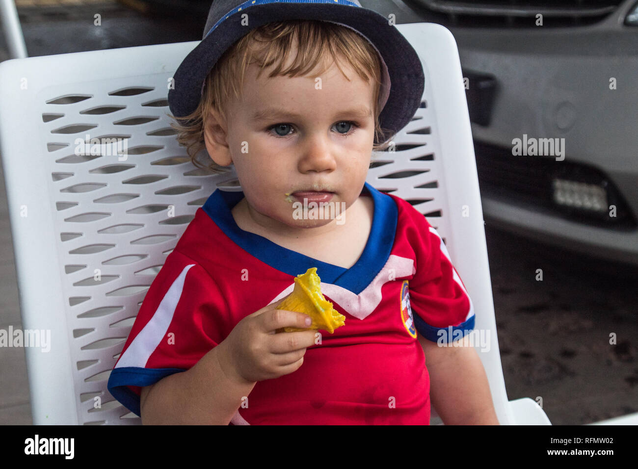 A portrait of a lovely boy with a blue hat enjoying a delicious ice cream. He is holding a yellow ice cream cone in his hand. Stock Photo