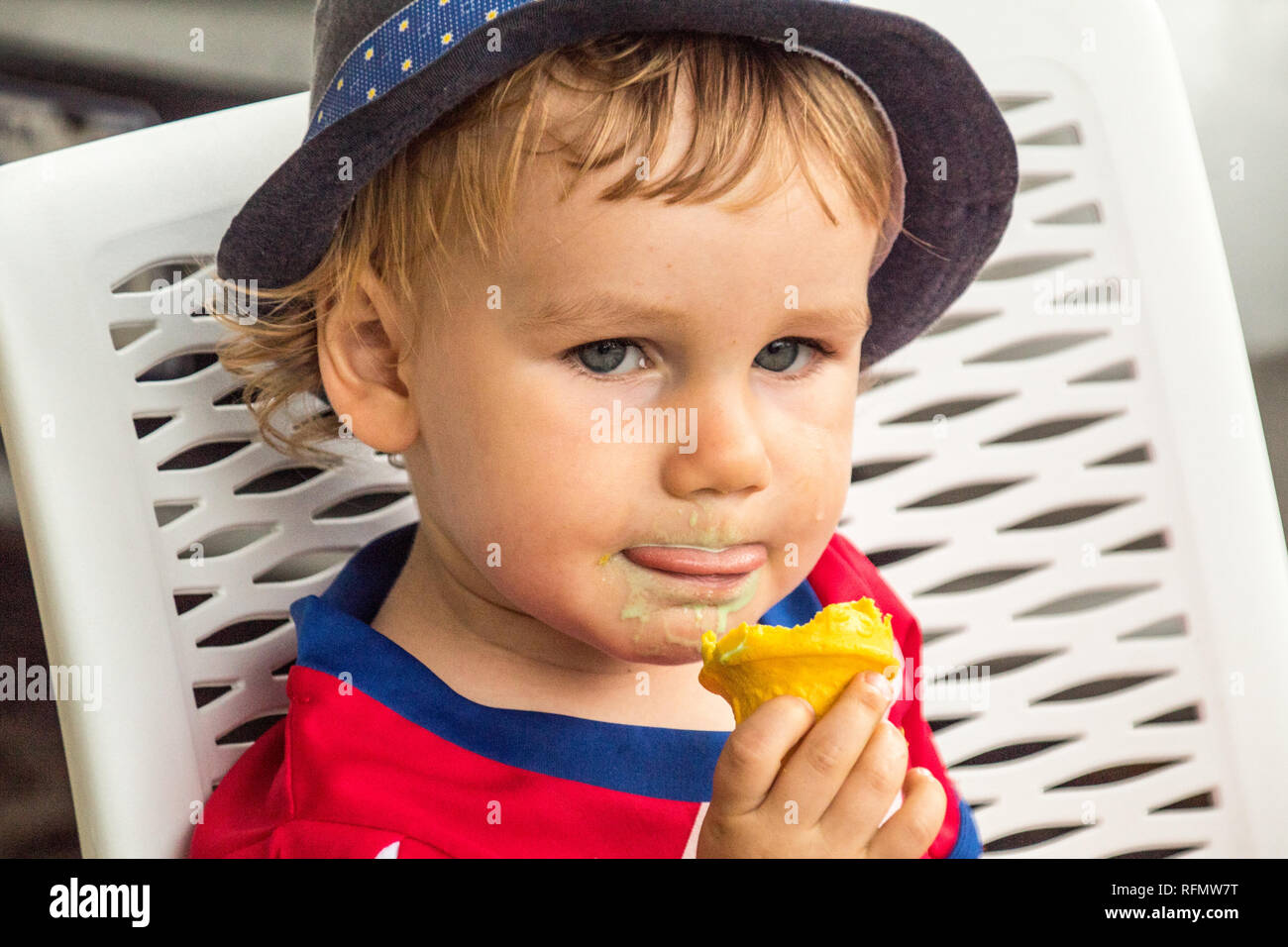 A portrait of a lovely boy with a blue hat enjoying a delicious ice cream. He is holding a yellow ice cream cone in his hand. Stock Photo