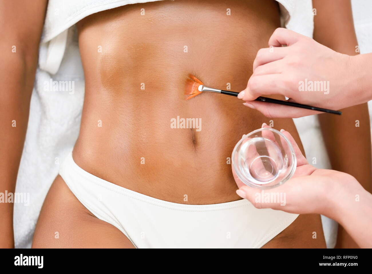 Woman receiving belly massage treatment with oil brush in spa wellness center. Beauty and Aesthetic concepts. Stock Photo