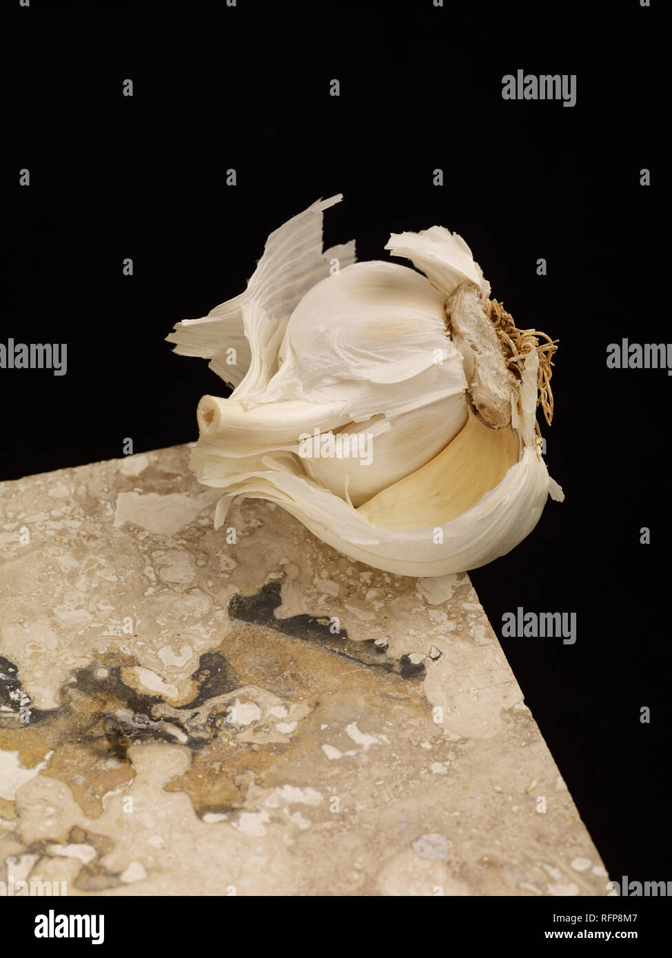 Garlic clove balanced on marble shelf against a black background, vegetable food photograph Stock Photo