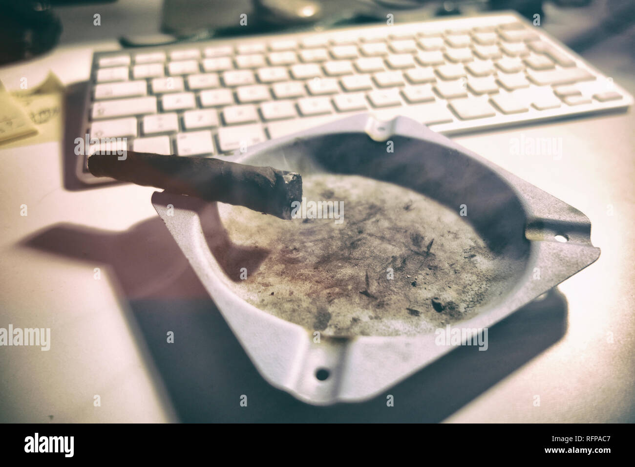 Toscano cigar burning on an ashtray. Computer keyboard in the background. Stock Photo