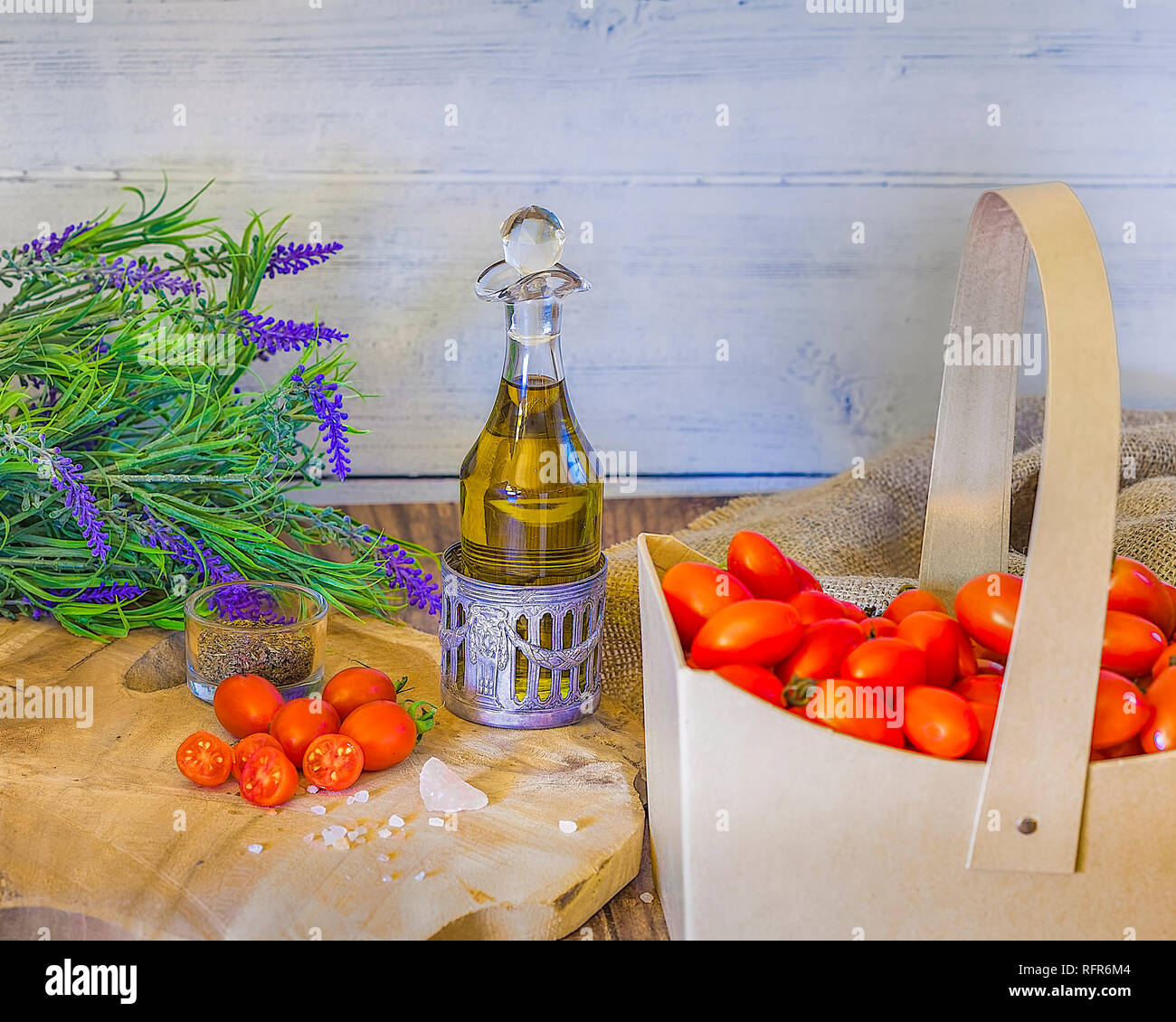 Cherry tomatoes in a cardboard  basket   with thyme,  olive oil , Himallayan pink salt on a wooden surface . Lavender flowers in the background. stock Stock Photo