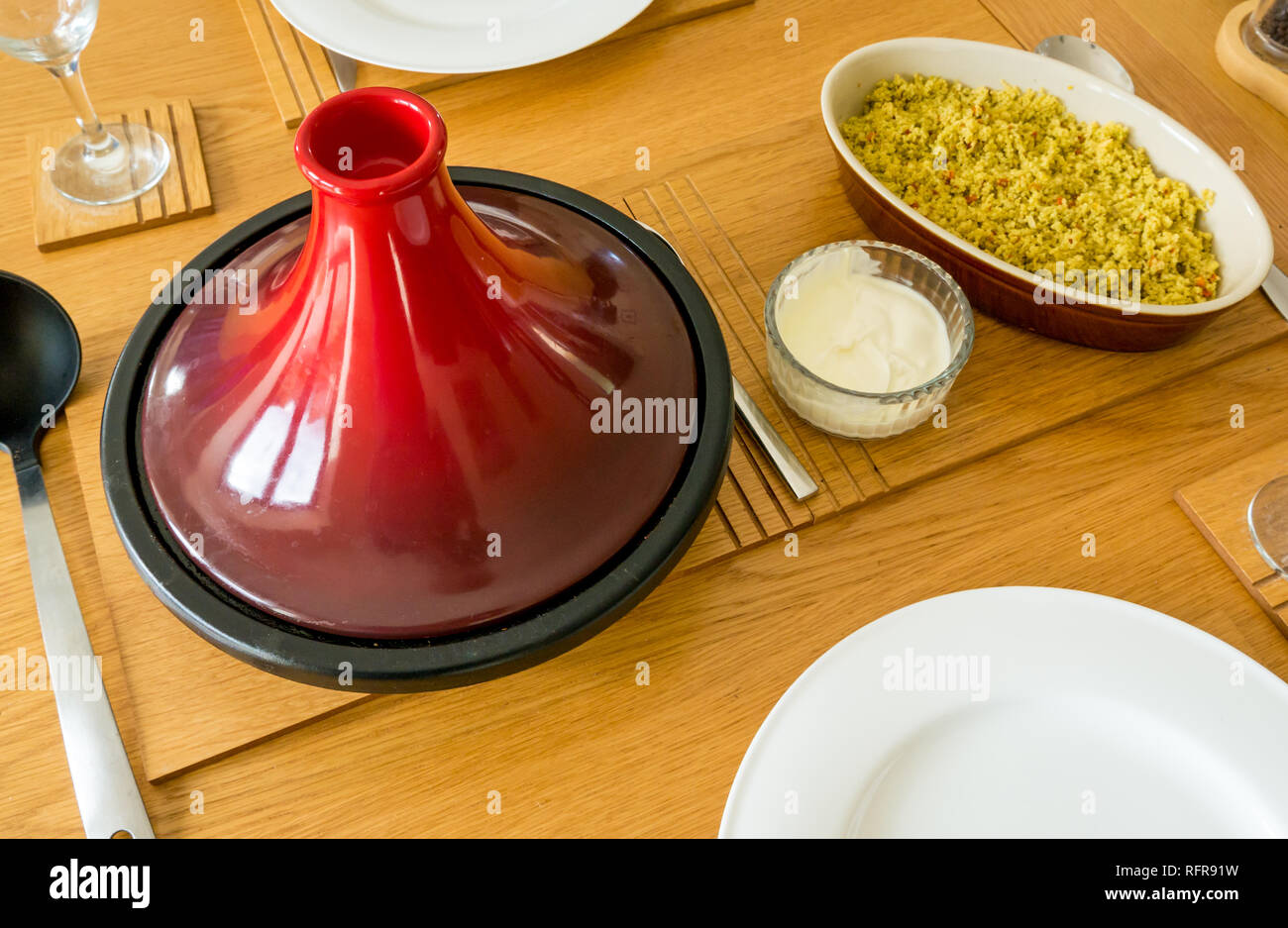 Red ceramic and cast iron tagine on oak table with serving ladle