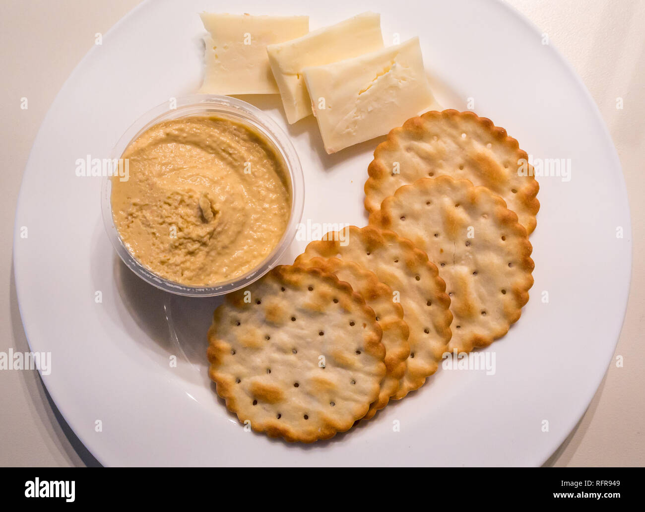 Close up of white plate with snack of round crackers, hummus and  cheddar cheese Stock Photo