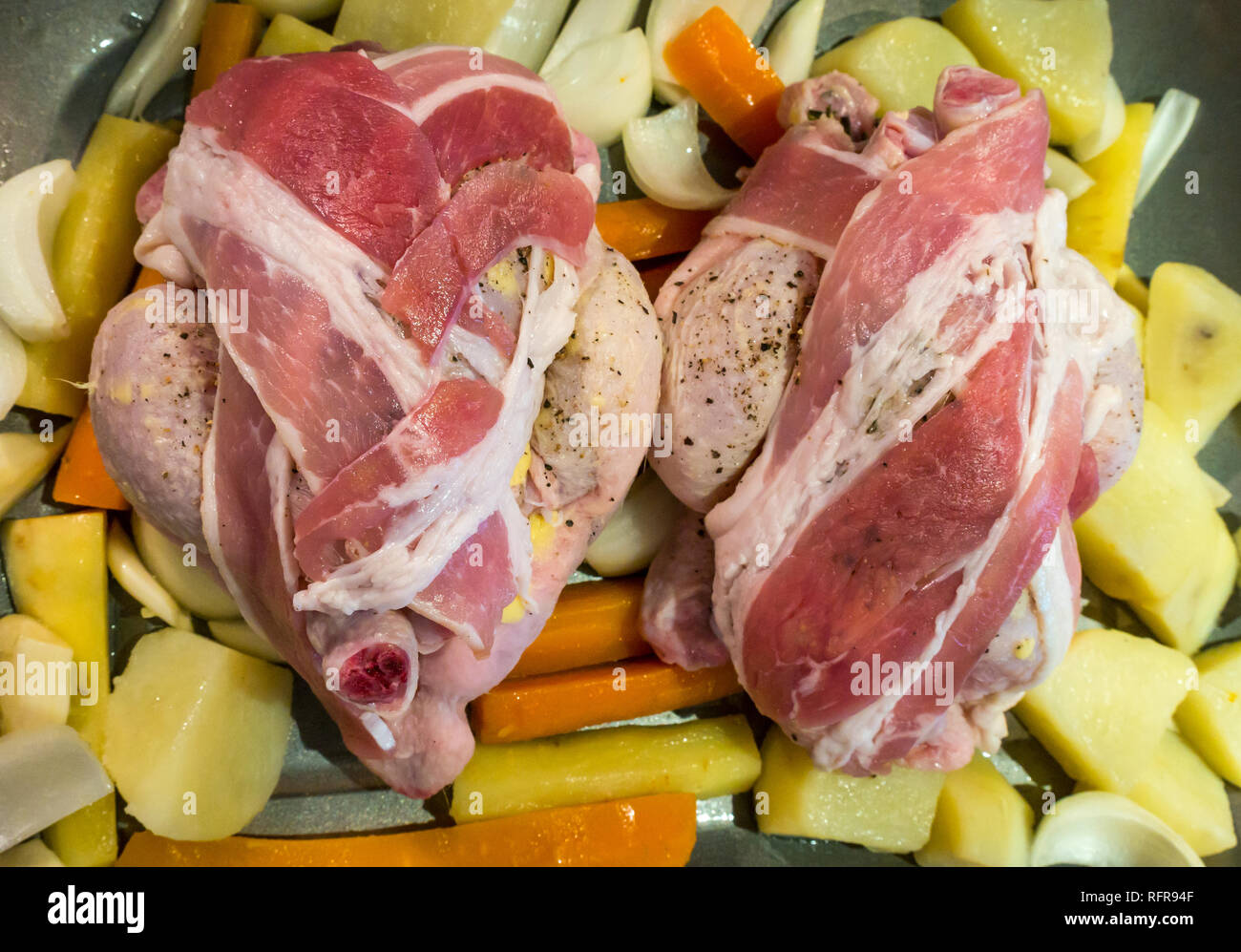 Two uncooked poussin wrapped in streaky bacon on a bed of vegetables ready for roasting in the oven Stock Photo