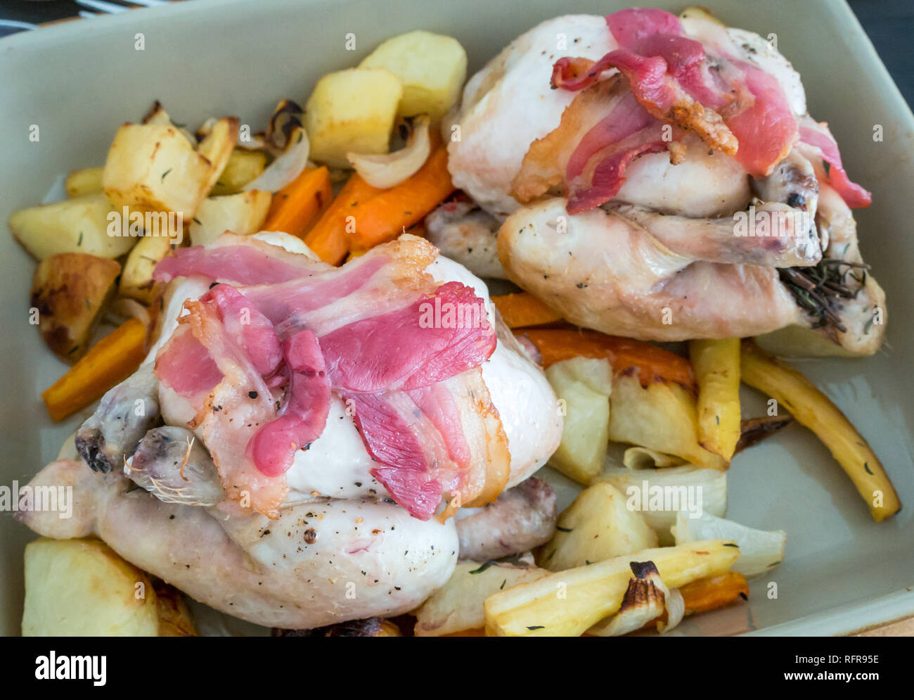 Close up of two uncooked poussin wrapped in streaky bacon on bed of vegetables ready for roasting in the oven Stock Photo