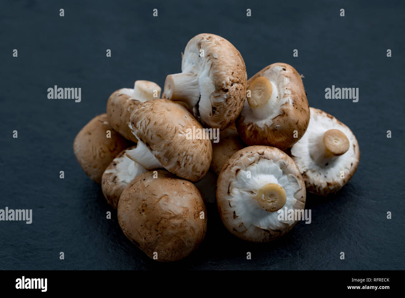 A heap of chestnut mushrooms bought from a supermarket in the UK photographed on a dark, stone background. Dorset England UK GB Stock Photo
