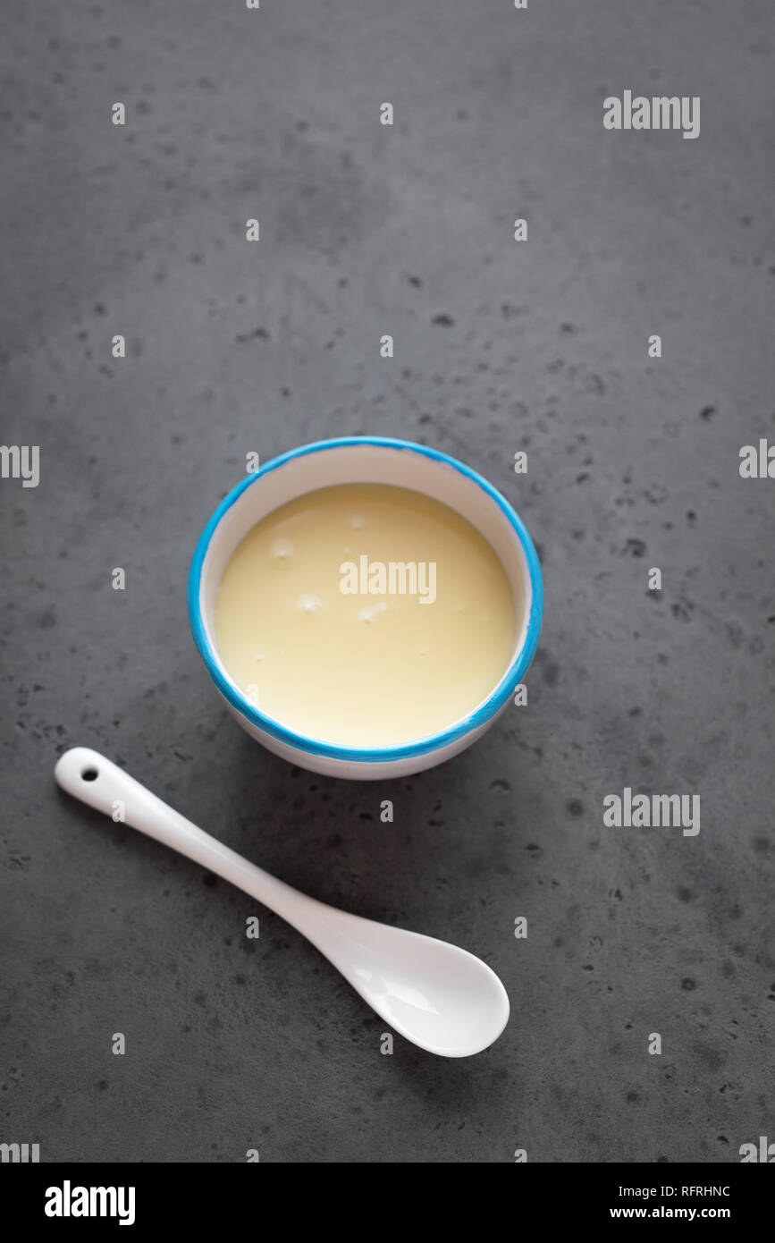 Condensed milk in white bowl. Sweet vanilla sauce, condensed or evaporated milk, top view, copy space. Stock Photo
