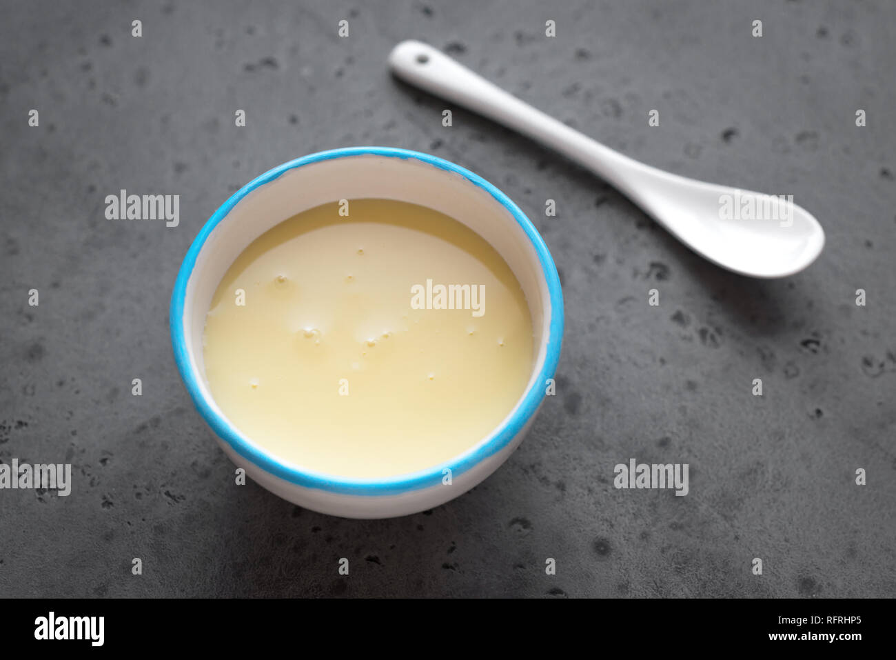 Condensed milk in white bowl. Sweet vanilla sauce, condensed or evaporated milk, top view, copy space. Stock Photo