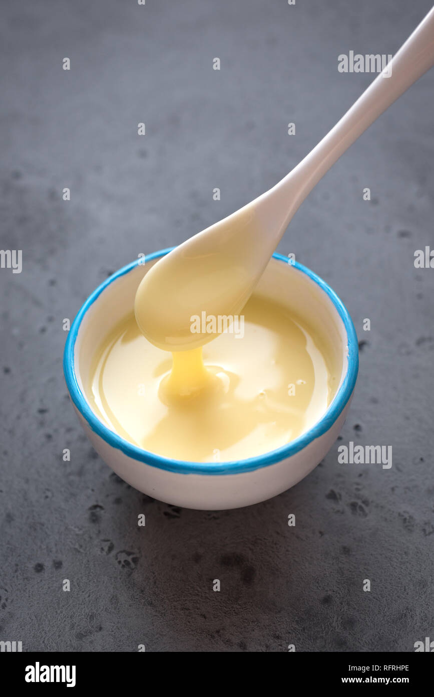 Condensed milk pouring in white bowl. Sweet vanilla sauce, condensed or evaporated milk, top view, copy space. Stock Photo