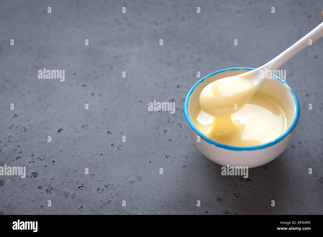 Condensed milk pouring in white bowl. Sweet vanilla sauce, condensed or evaporated milk, top view, copy space. Stock Photo