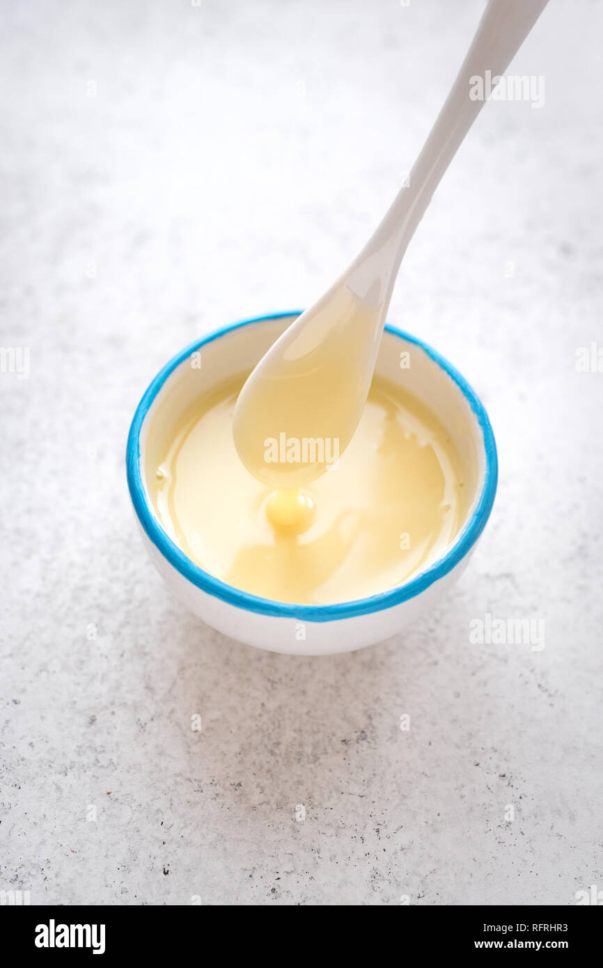 Condensed milk pouring in white bowl. Sweet vanilla sauce, condensed or