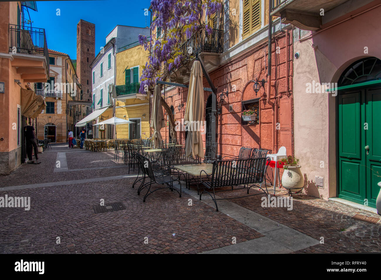 Colorful old buildings on a cobbled street with restaurant tables and chairs in Noli, Savona, Liguria, Italy in morning light Stock Photo