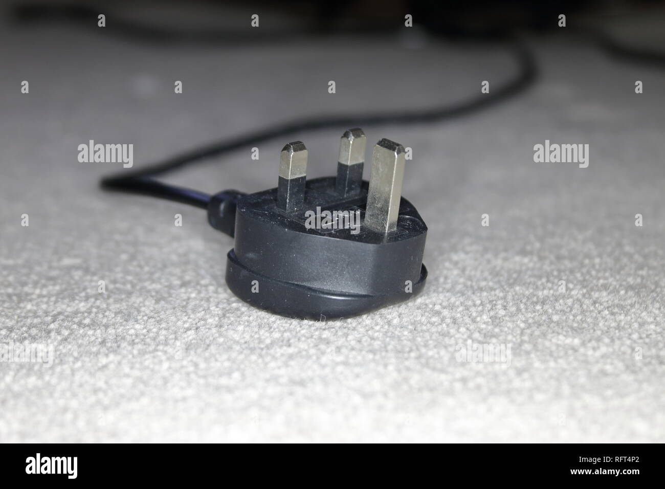 uk fused 3 pin moulded electric power plug and cable unplugged and left with the pins upper most on a carpet Stock Photo