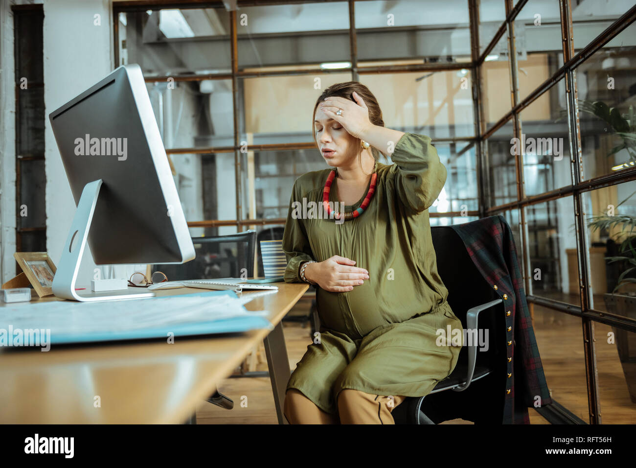 Pregnant woman sitting in the office feeling awful and anxious Stock Photo