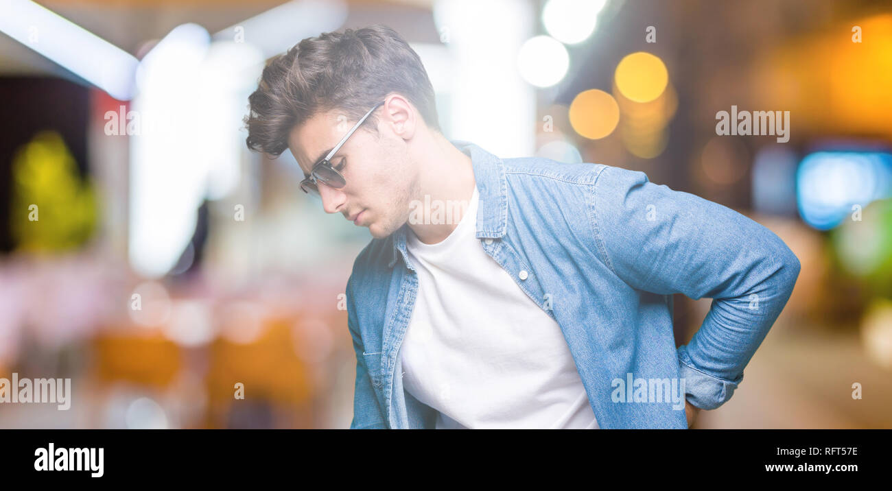 Young handsome man wearing sunglasses over isolated background Suffering of backache, touching back with hand, muscular pain Stock Photo