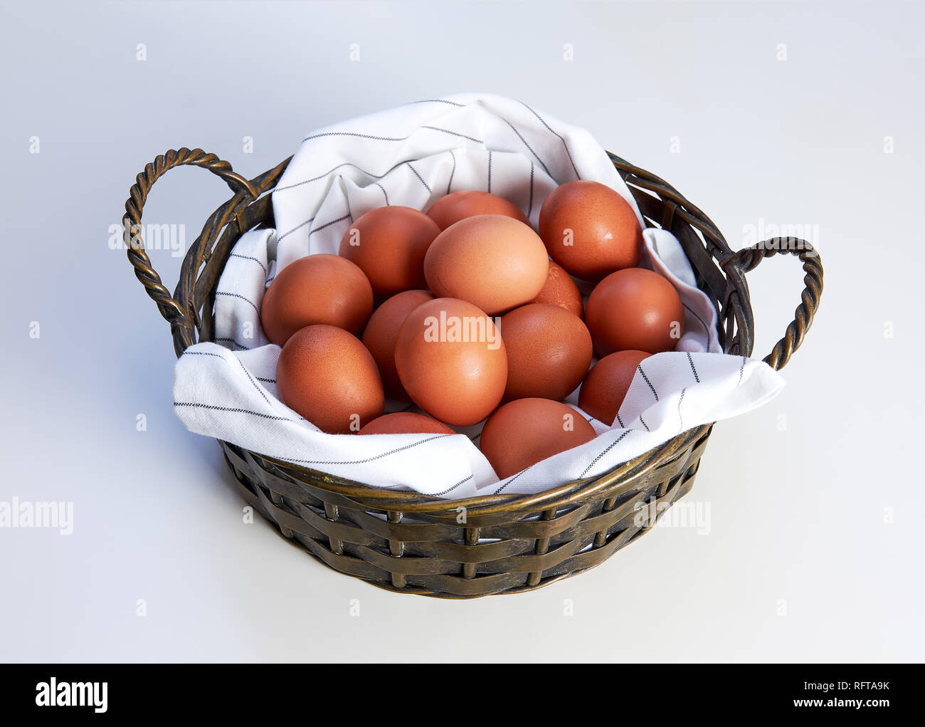Metal basket with towel and heap of hen eggs on a white background Stock Photo