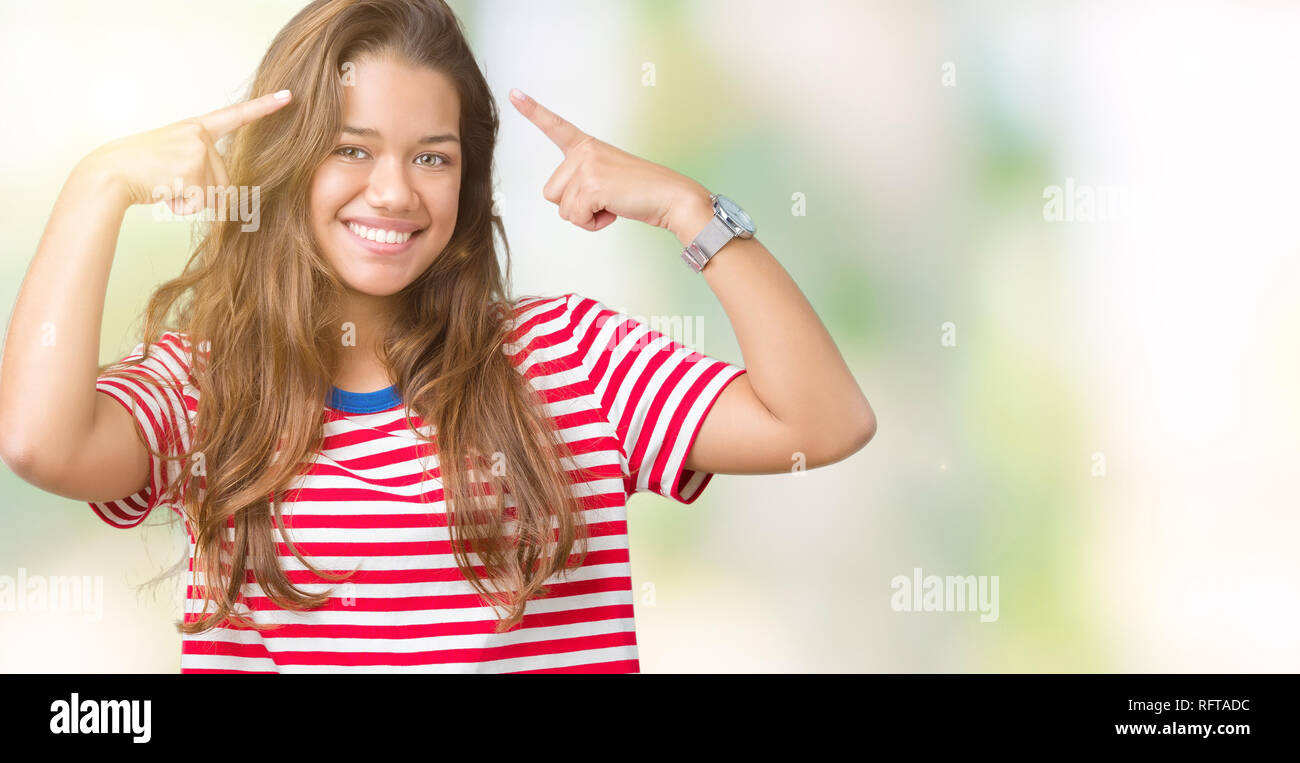 Young beautiful brunette woman wearing stripes t-shirt over isolated background Smiling pointing to head with both hands finger, great idea or thought Stock Photo