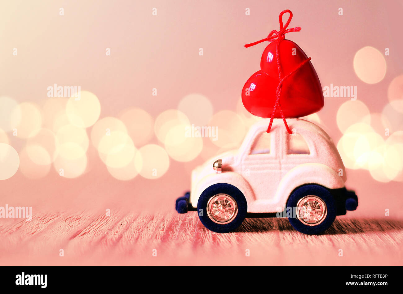 Little pink car carries a red heart. The concept of Valentine Day. Stock Photo