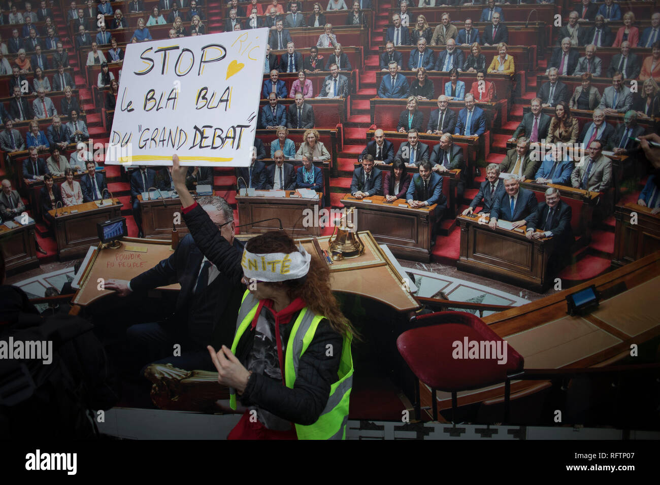 A protestor stands in front of an image of the parliament while holding a placard during a demonstration against macron policies. Yellow vest protestors gathered and march on the streets of Paris another Saturday on what they call the Act XI against the French president Emmanuel Macron policies. Stock Photo