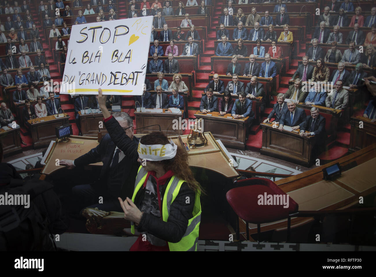 Paris, Ile de France, France. 26th Jan, 2019. A protestor stands in front of an image of the parliament while holding a placard during a demonstration against macron policies. Yellow vest protestors gathered and march on the streets of Paris another Saturday on what they call the Act XI against the French president Emmanuel Macron policies. Credit: Bruno Thevenin/SOPA Images/ZUMA Wire/Alamy Live News Stock Photo