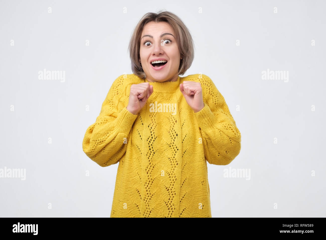 Pretty shocked woman in yellow sweater screaming and clenching her fists. I  can not believe my luck Stock Photo - Alamy