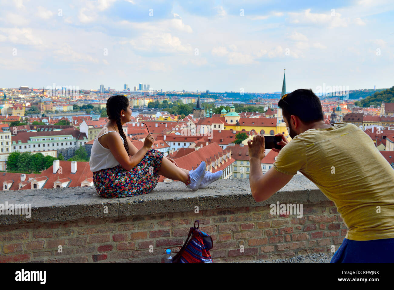 View overlooking city of Prague from castle with man taking photography of woman sitting on wall Stock Photo