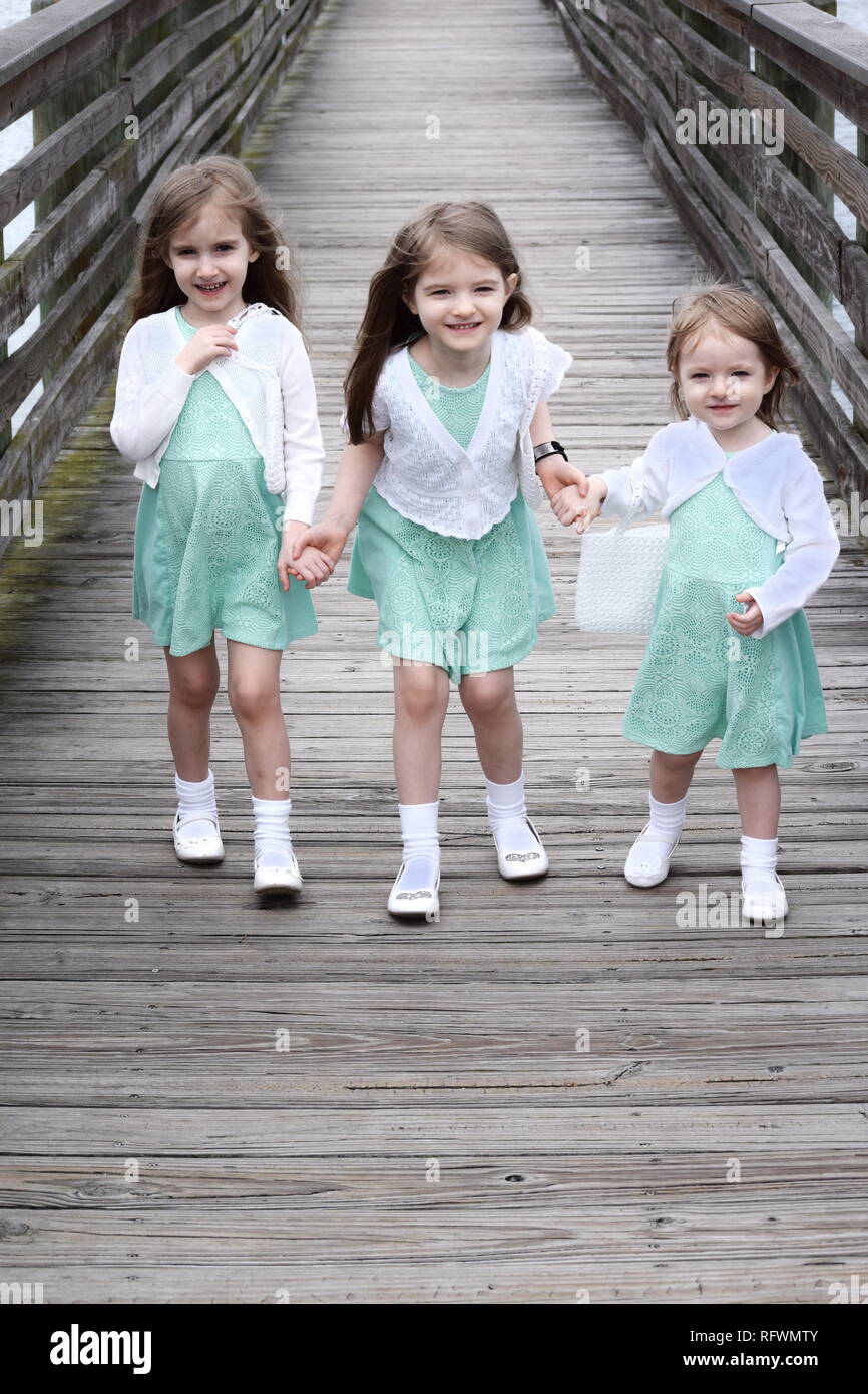 Three Young sisters running on pier outdoors holding hands happy and smiling with matching dresses Stock Photo Alamy