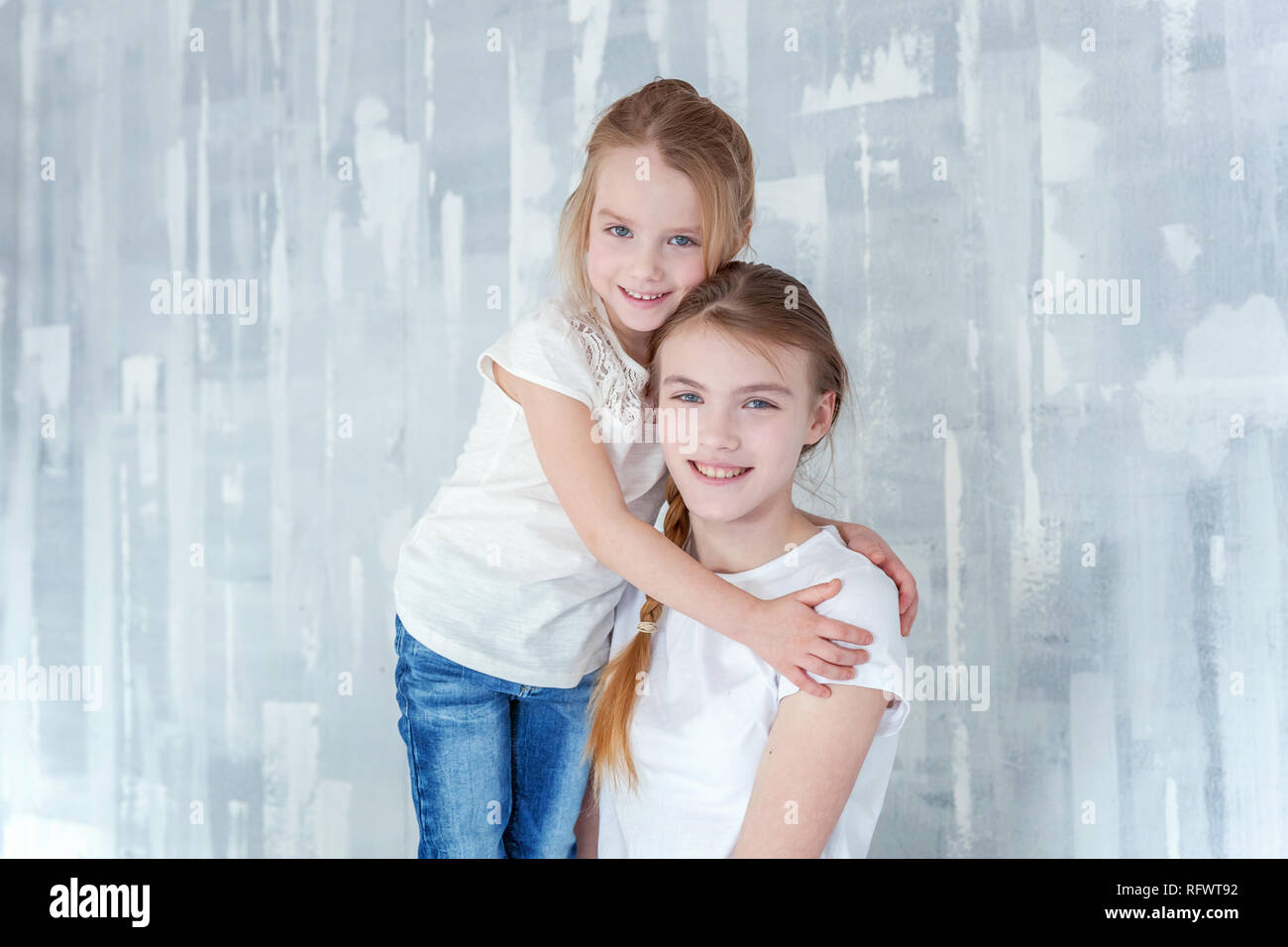 Two happy kids standing against grey textured wall background and ...