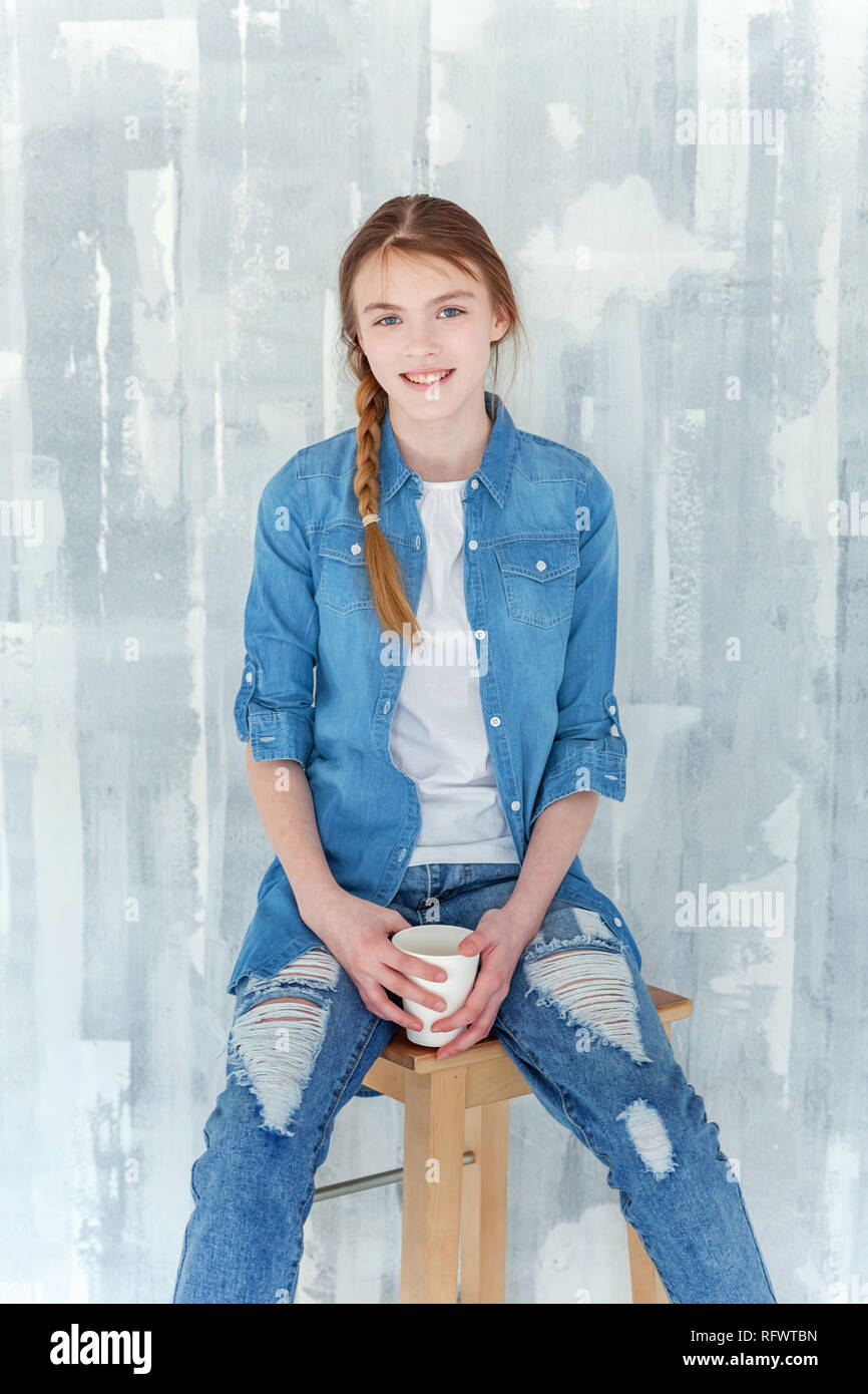 Young happy cute teenage girl in jeans, denim jacket and white T-shirt  sitting on chair against grey textured wall background, holding paper cup  and d Stock Photo - Alamy