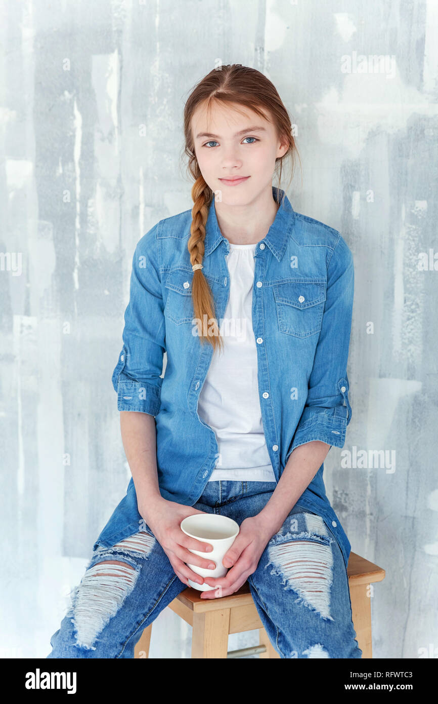 Young happy cute teenage girl in jeans denim jacket and white Tshirt  sitting on chair against grey textured wall background holding paper cup  and d Stock Photo  Alamy