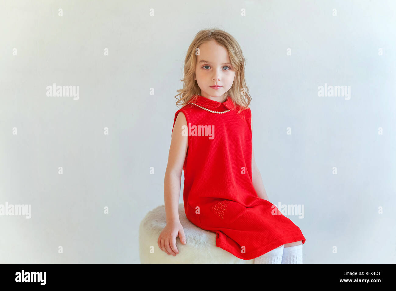 Sweet happy little girl in red dress sitting on chair against white ...
