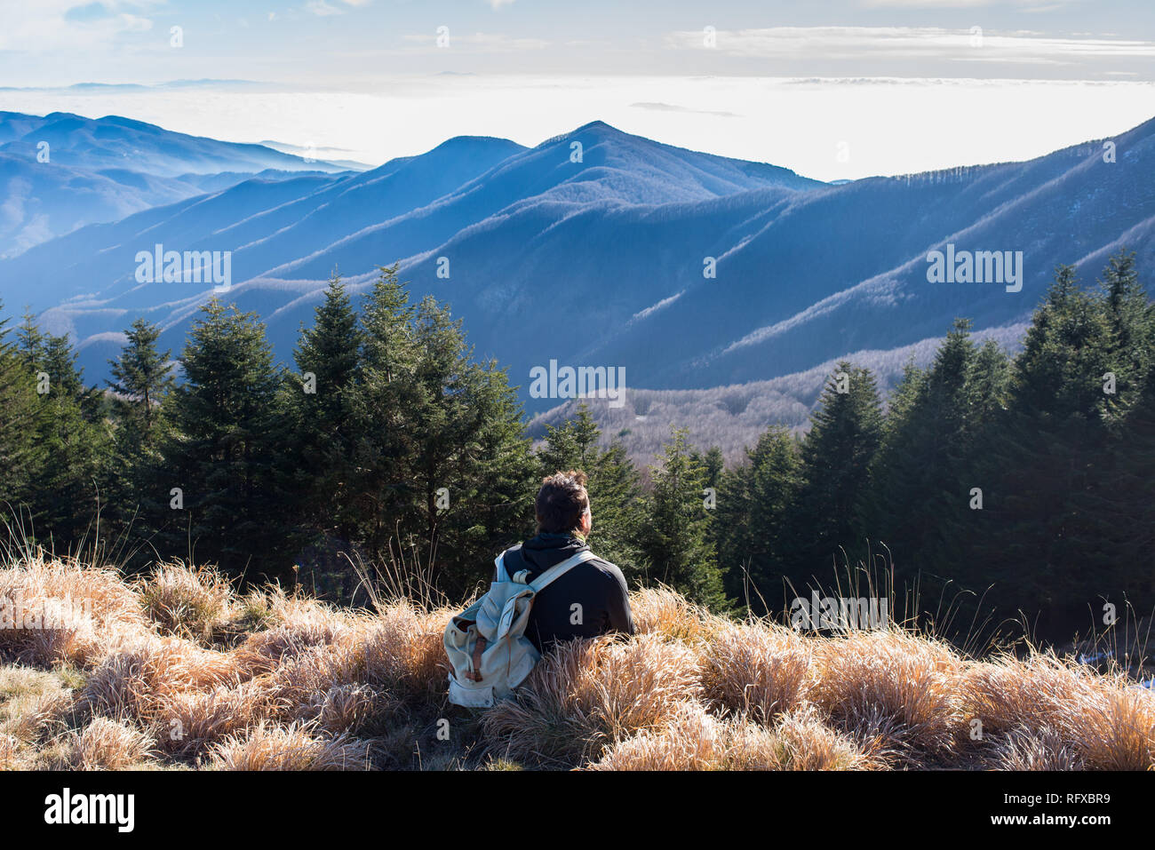 One man hiker wearing vintage rucksack sitting alone admiring the mountain landscape in winter. Stock Photo