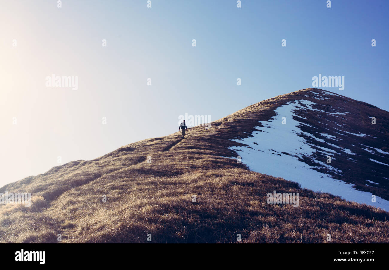 One Man hiker hiking alone climbing down a steep mountain path in winter. Taken from distance. Matte high contrast effect Stock Photo