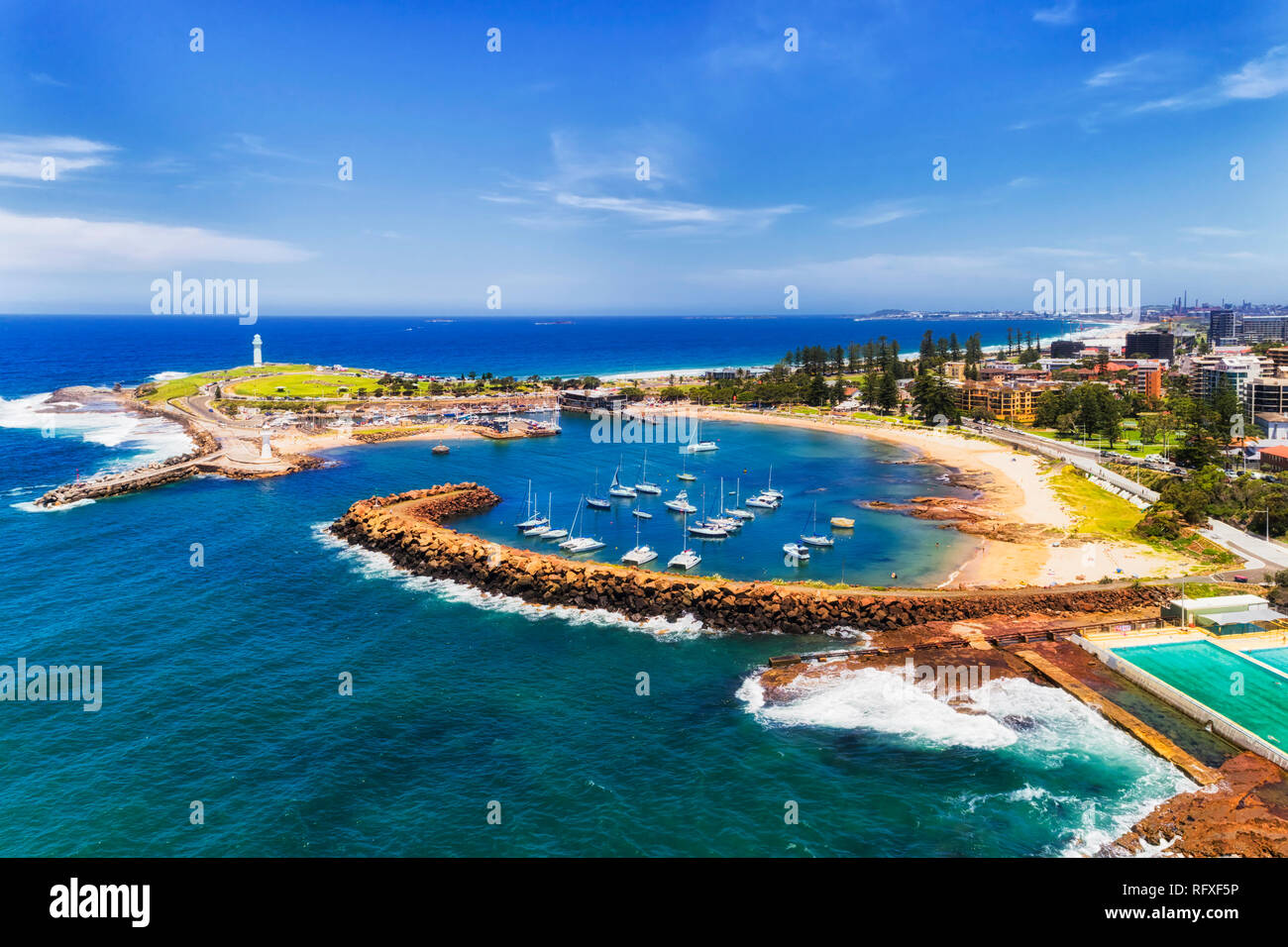 Protected Wollongong town harbour with marina and moored yachts behind sandstone breakwater wall and two white lighthouses with sandy beach on town co Stock Photo
