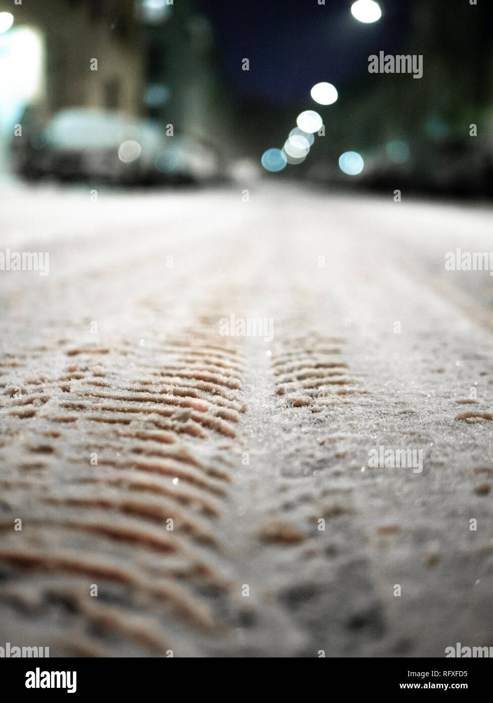 Close up shot of snowy street with tire marks, cars and street lights in background out of focus Stock Photo