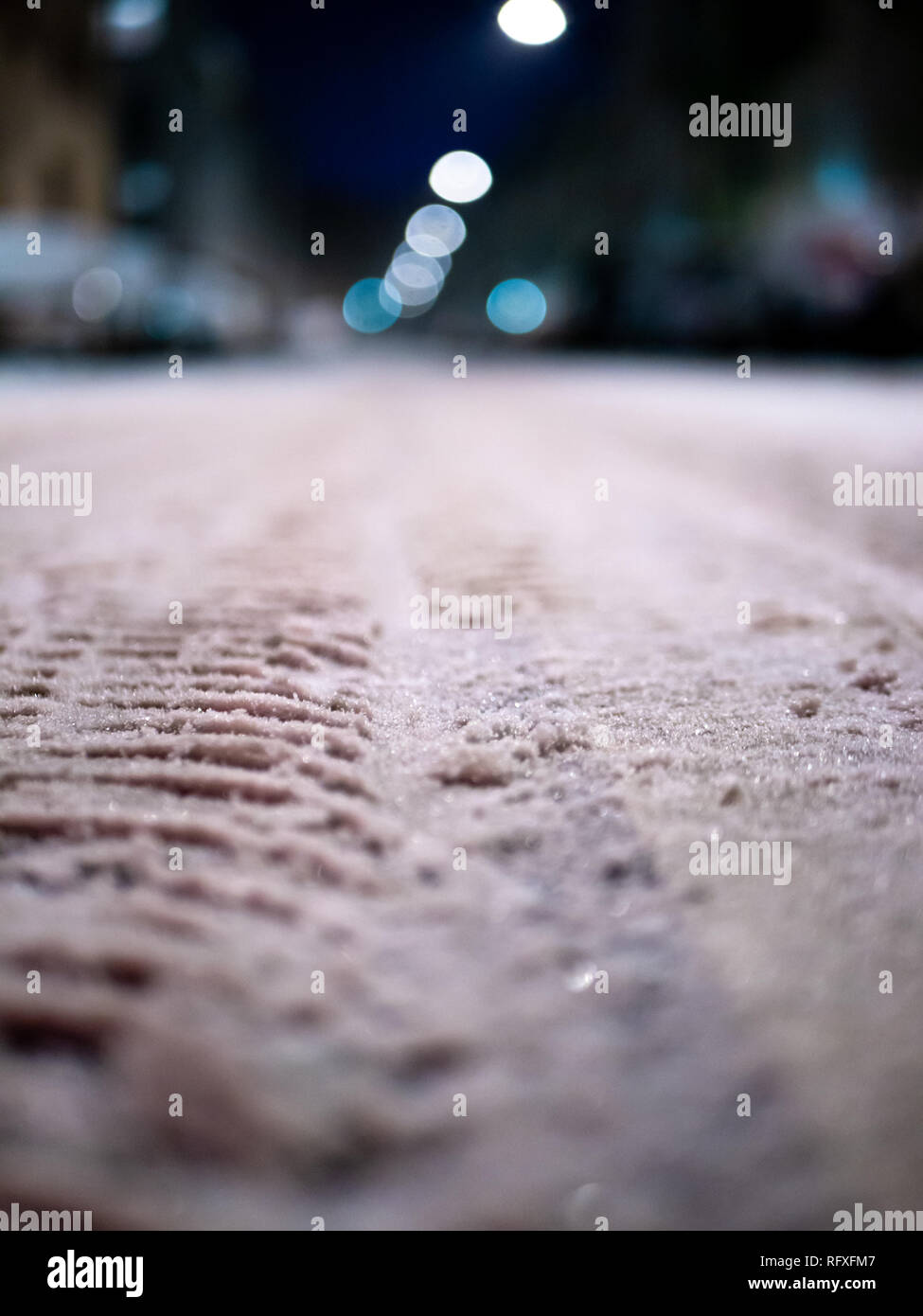 Close up shot of snowy street with tire marks, cars and street lights