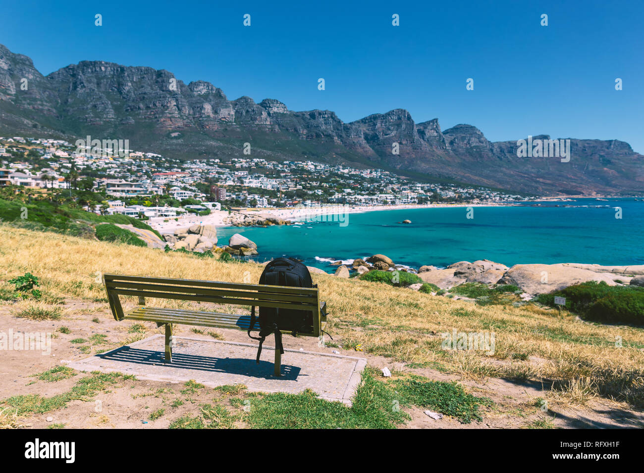 Backpack of lonely traveller on a bench with a view of Camps bay beautiful beach in Cape Town, South Africa Stock Photo