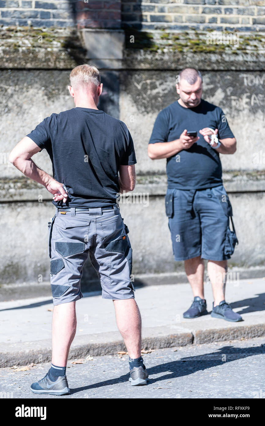 London, UK - September 13, 2018: Street in Belgravia area with candid men two security guards standing looking at phones on pavement vertical view Stock Photo