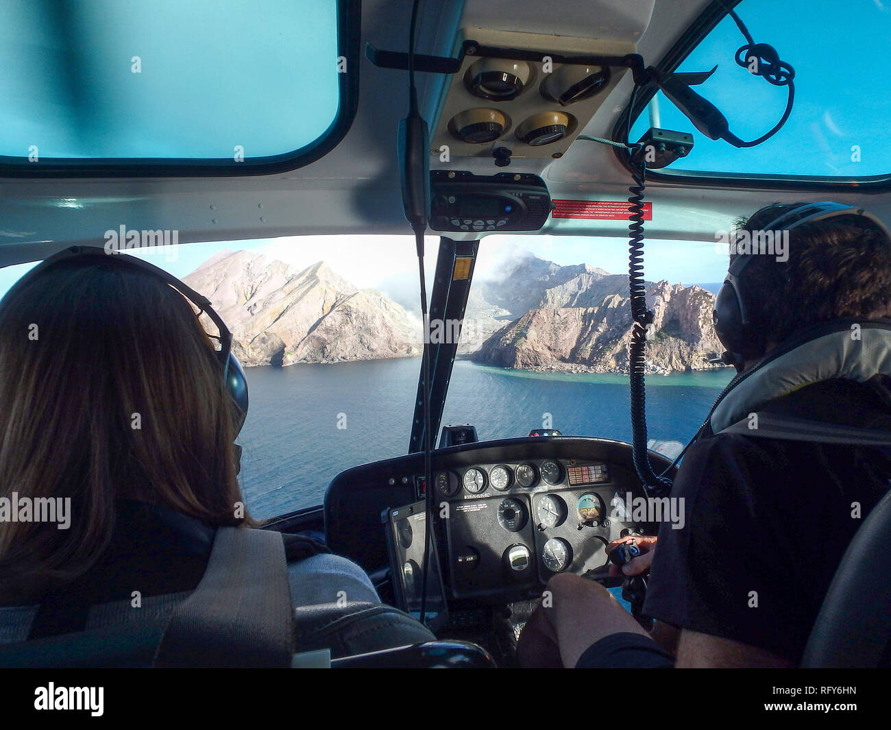 A male helicopter pilot and a female passenger flying towards the active volcano of Whakaari, White Island, New Zealand. Over-the-shoulder view. Stock Photo
