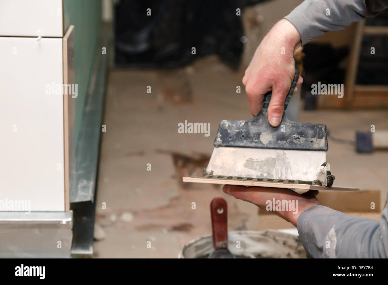 Closeup builder's hand smears cement glue on the ceramic tile with