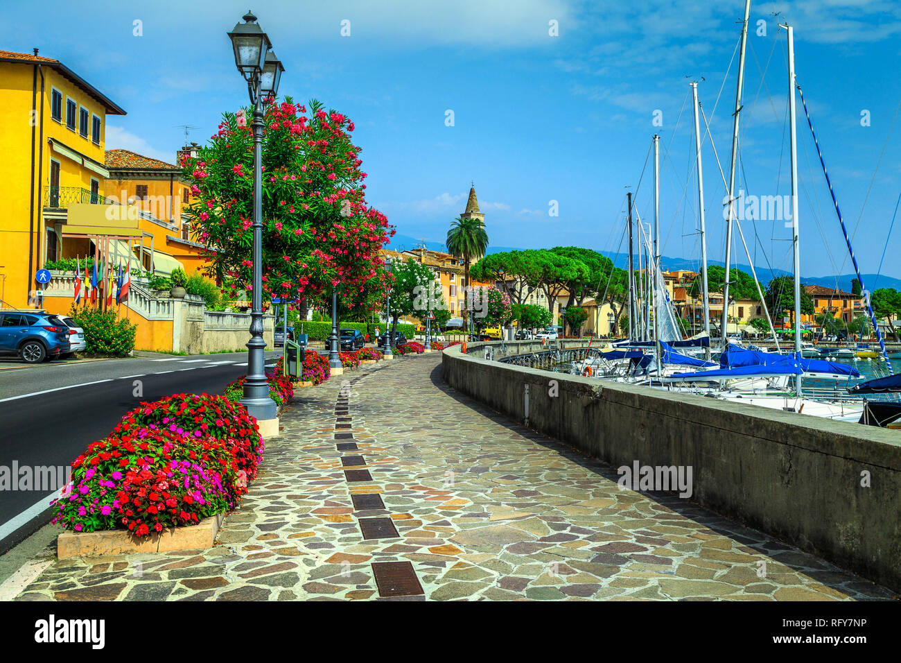 Amazing paved promenade with colorful mediterranean flowers. Luxury yachts, boats and sailing boats in the stunning harbor of Toscolano-Maderno, lake  Stock Photo