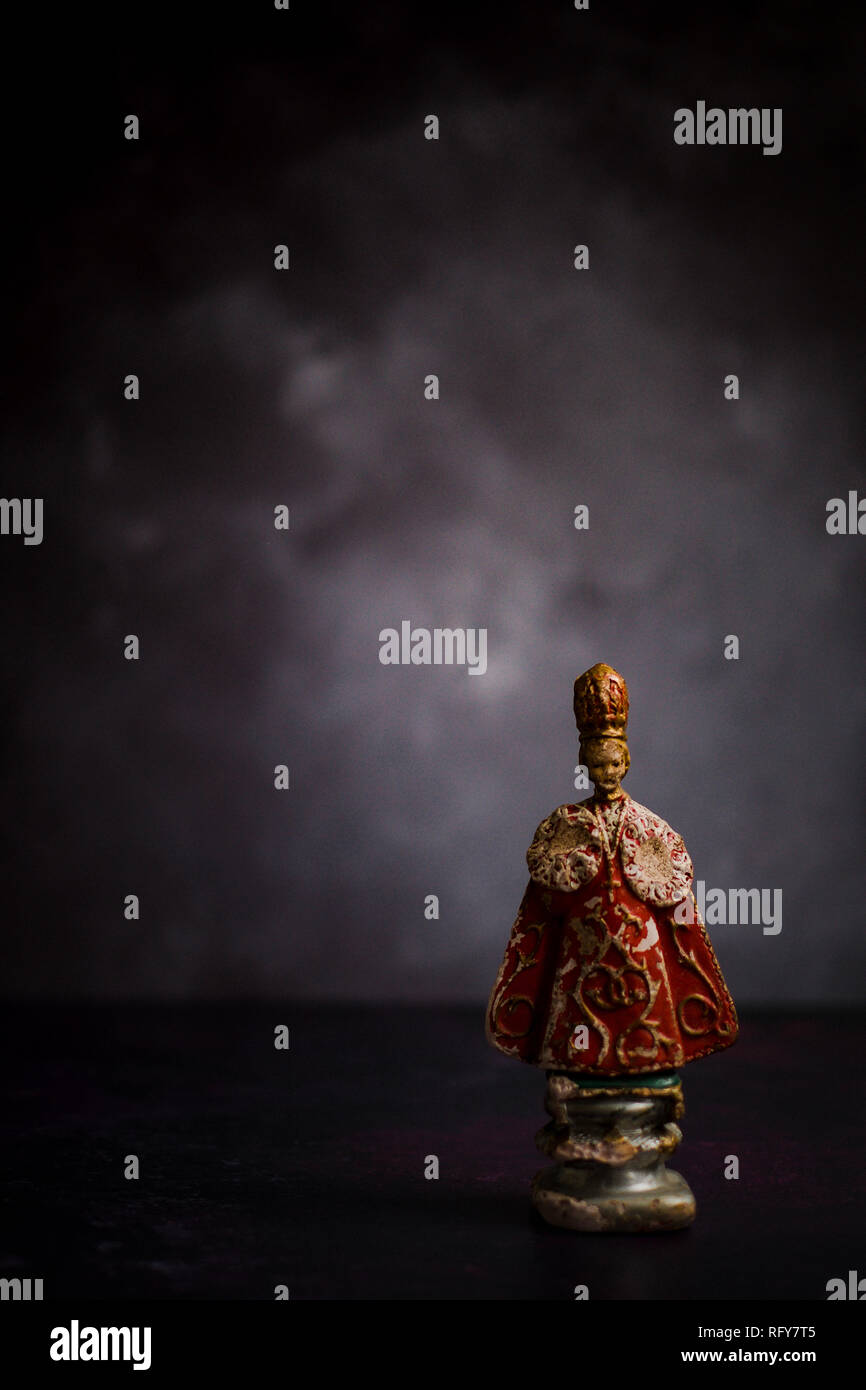 Antique statue of the Infant Jesus of Prague, against a dark background. The original statue is a 16th-century wax-coated wooden statue of the Christ  Stock Photo